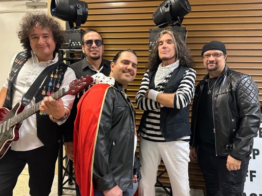 Five musicians posing together, wearing leather jackets, with instruments and stage lights.